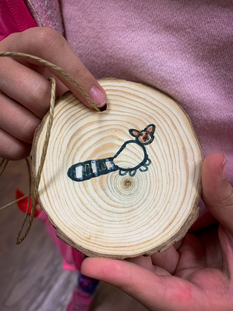 A girl holding a tree cookie with a ringtail drawn on it. 